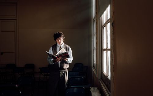 Free A teenager reads a book by the window in a Buenos Aires classroom, creating a serene and studious atmosphere. Stock Photo
