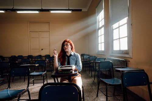 Free A lone student with red hair sits in an empty classroom in Buenos Aires, holding a pen. Stock Photo