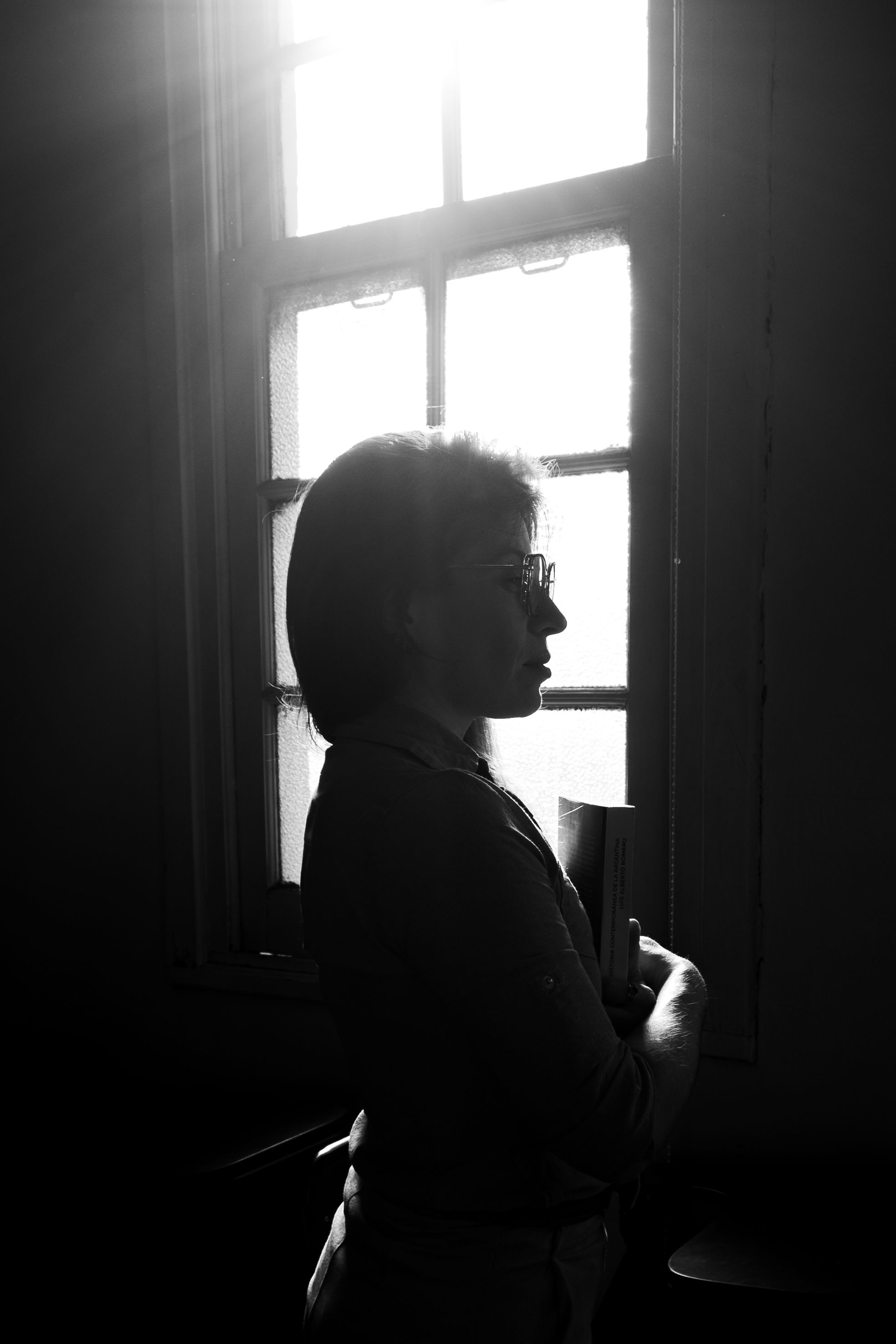 A black and white silhouette of a woman standing by a window, evoking mystery and contemplation.. black, white, silhouette