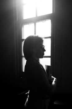 A black and white silhouette of a woman standing by a window, evoking mystery and contemplation.. black, white, silhouette
