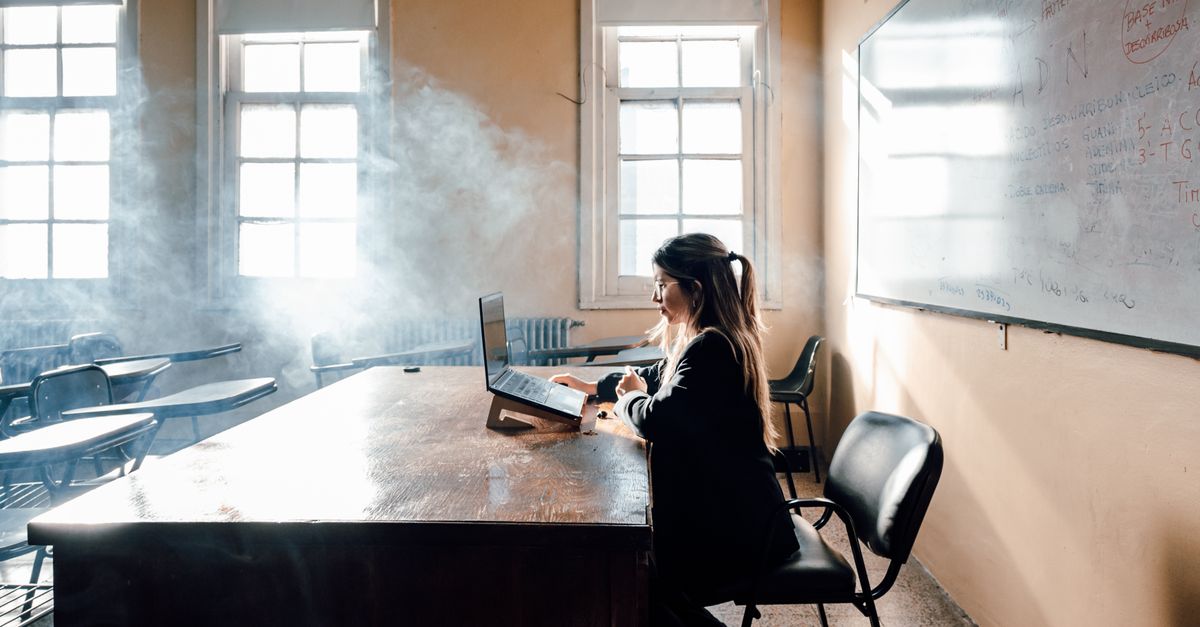 person turning off a laptop and closing it at a desk near a window at sunset