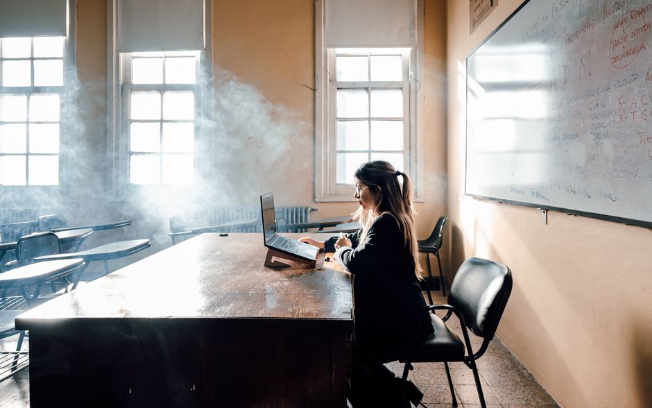 A student studies in a sunlit Buenos Aires classroom, surrounded by smoke and empty desks.