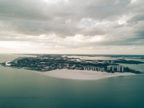 Scenic aerial view of coastal city and beach under a dramatic cloudy sky, showcasing urban and natural landscapes.