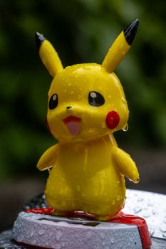 Adorable Pikachu toy with raindrops, standing on a surface, outdoors in nature.