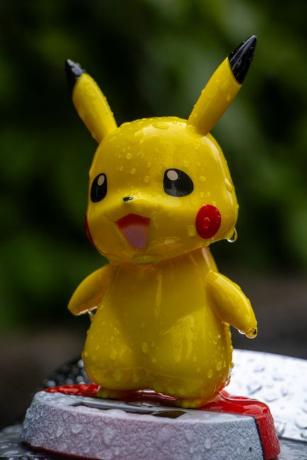 Adorable Pikachu toy with raindrops, standing on a surface, outdoors in nature.
