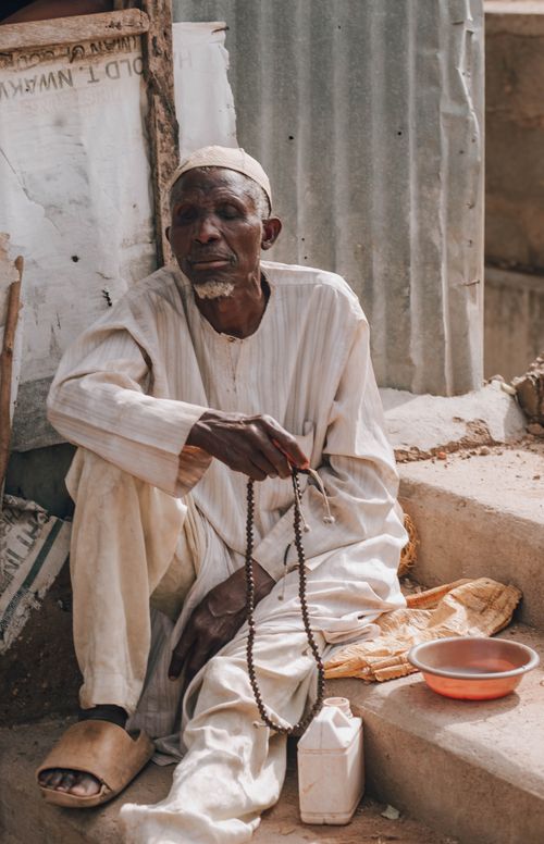 Free A senior man in traditional attire holding prayer beads seated outside on a concrete step. Stock Photo