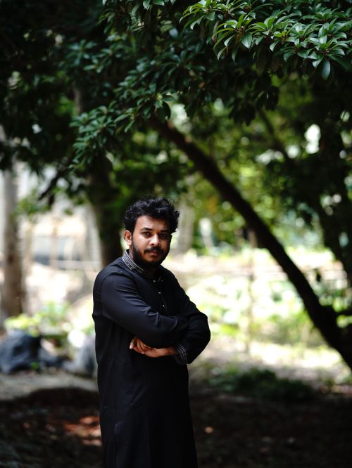 Free Man in traditional attire standing outdoors under lush greenery. Stock Photo