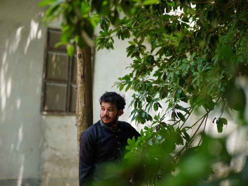 Free A man standing beside a tree with lush green leaves, outdoors. Stock Photo