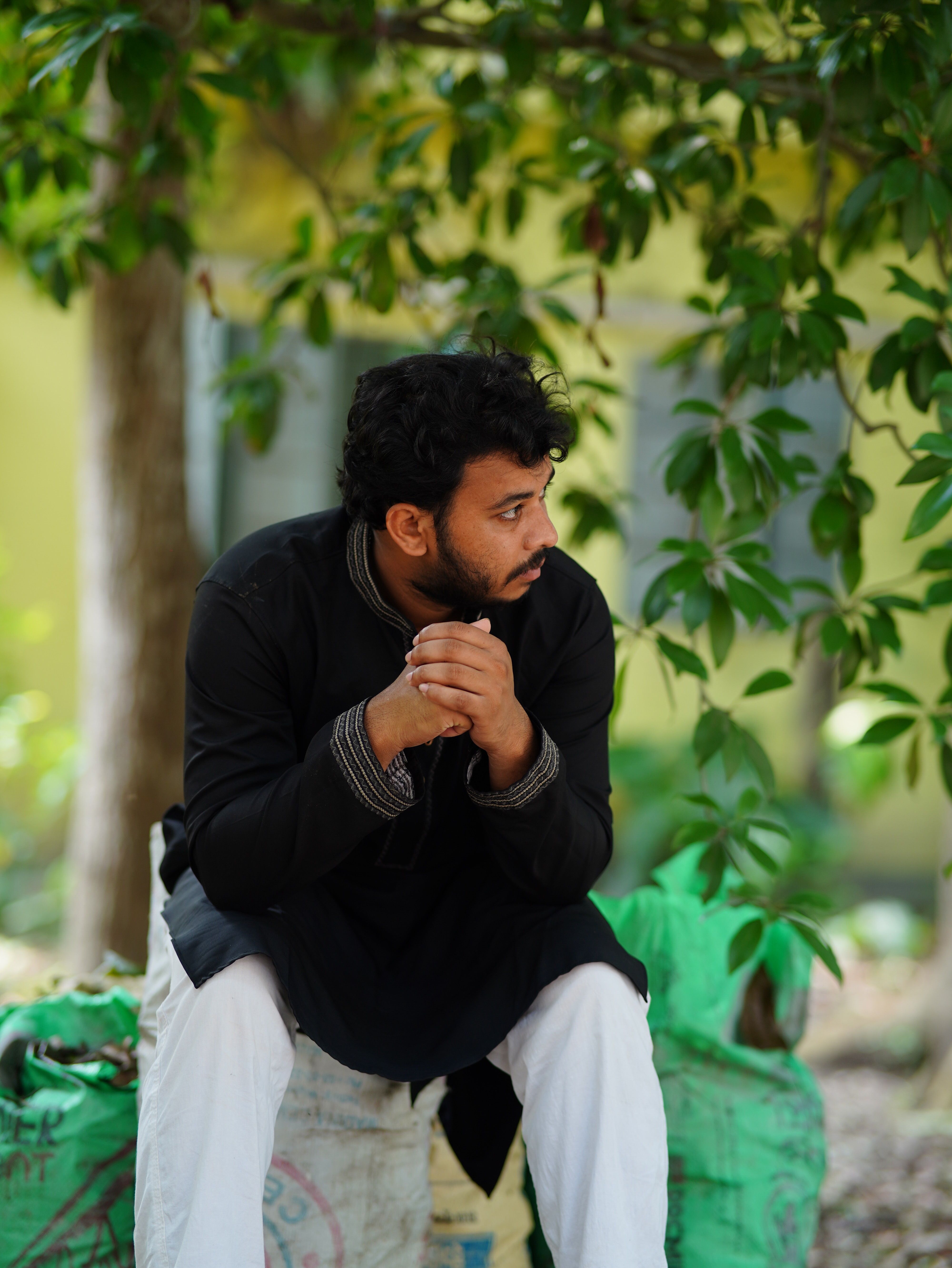 A man in traditional attire sits thoughtfully under a tree in Bangladesh.