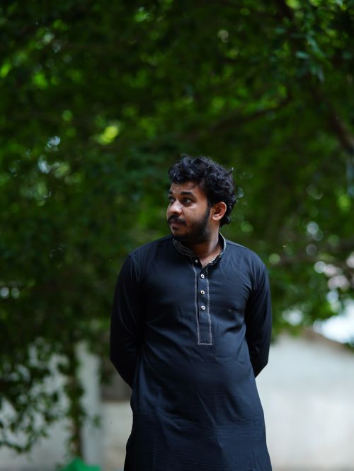 Free A man in traditional attire stands outdoors, surrounded by lush greenery. Stock Photo