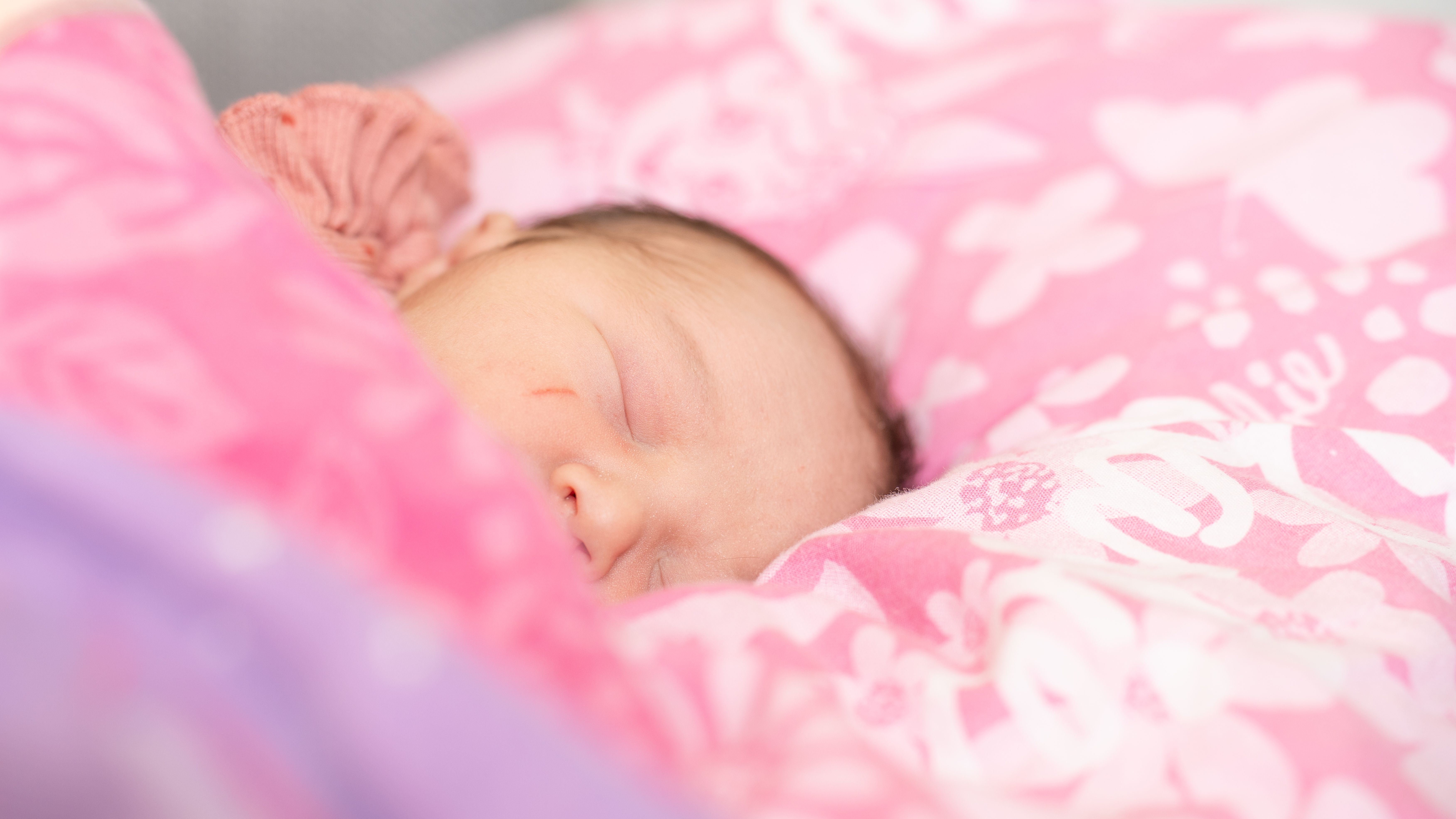 A serene portrait of a sleeping baby nestled on a pink-patterned pillow, capturing tranquility.