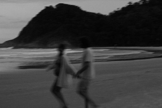 Blurred silhouette of a couple walking on a beach near hills during twilight, capturing a tranquil and romantic moment.
