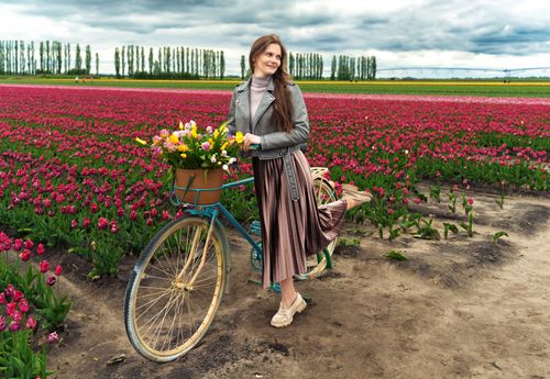 Free Woman stands next to a bicycle with flowers in a vibrant tulip field under cloudy skies. Stock Photo