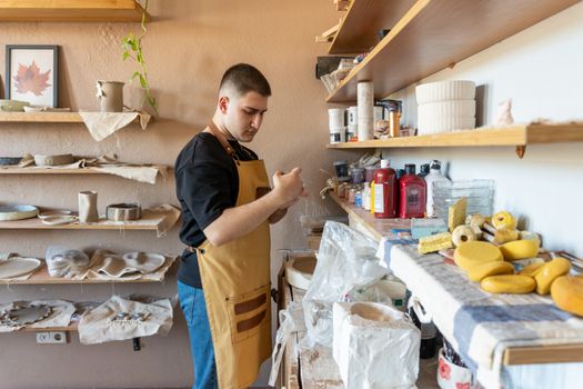 A young potter in a craft studio, focused on shaping clay. Shelves filled with pottery tools and supplies.