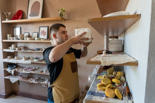 A potter arranges shelves with ceramic goods in a well-lit workshop, showing creativity and craftsmanship.