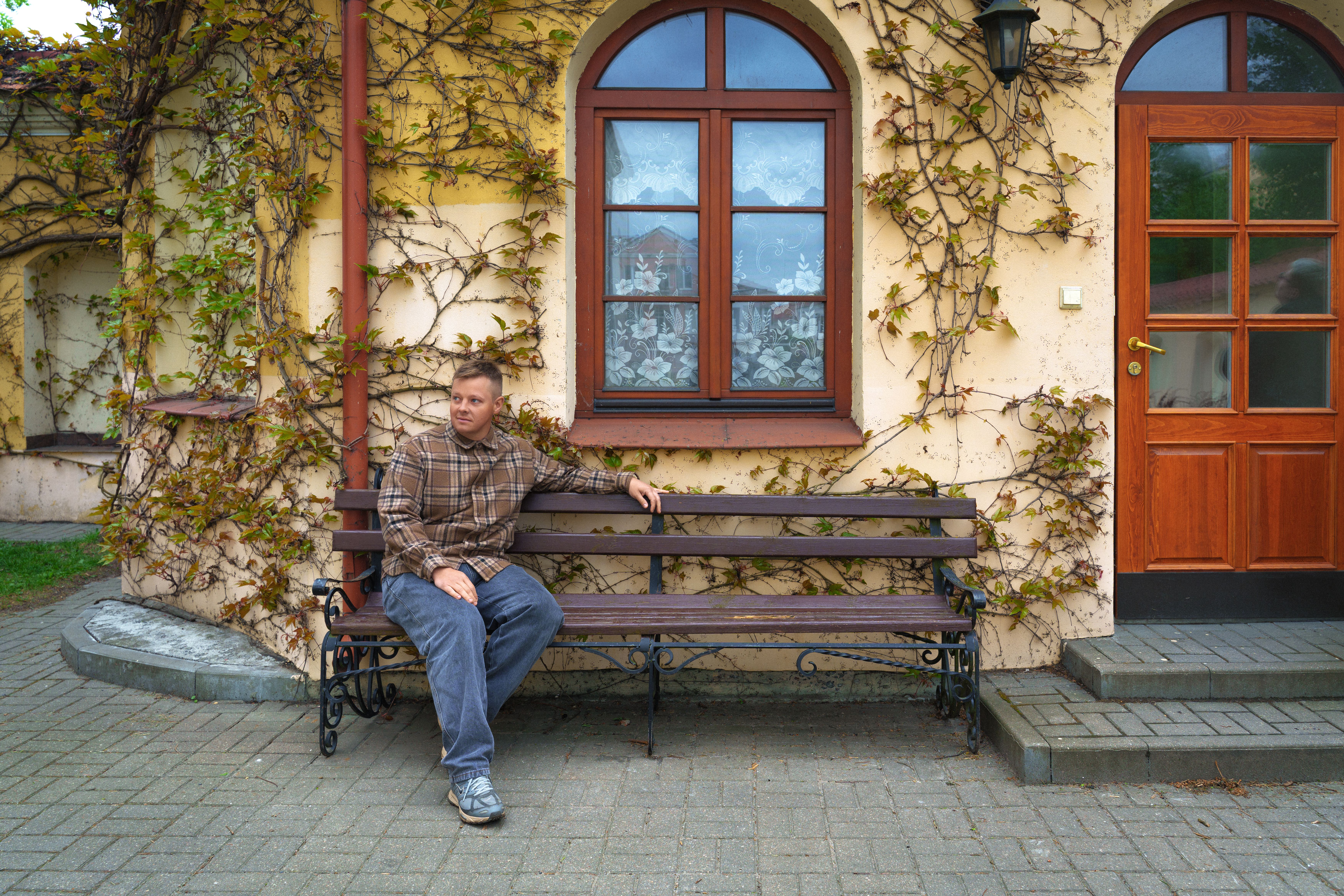 A man sitting on a bench beside an ivy-covered building in Pinsk, Belarus. Captured in an urban outdoor setting.