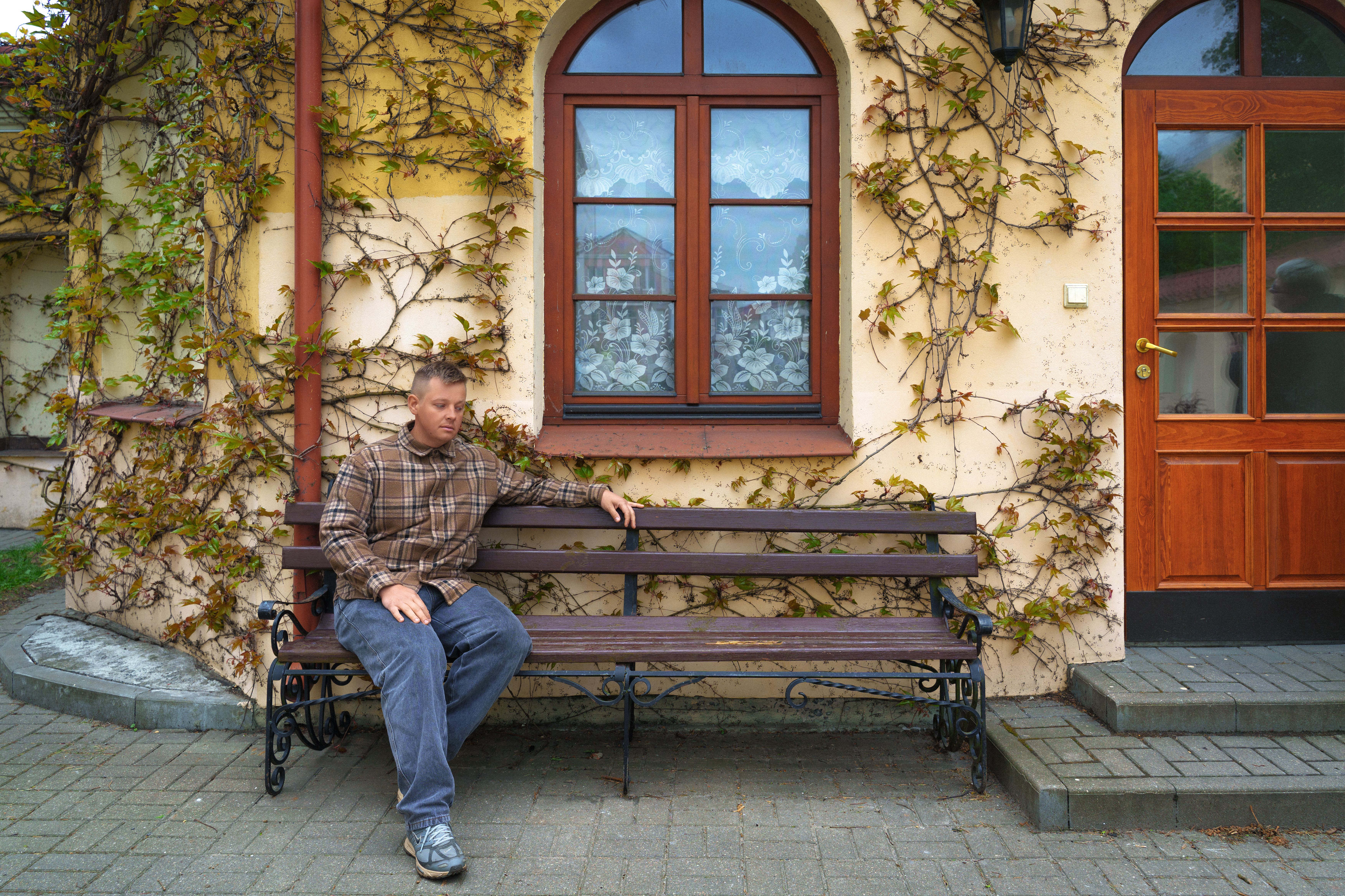Man sitting on a bench beside a vine-covered wall in Pinsk, Belarus, under a clear sky.