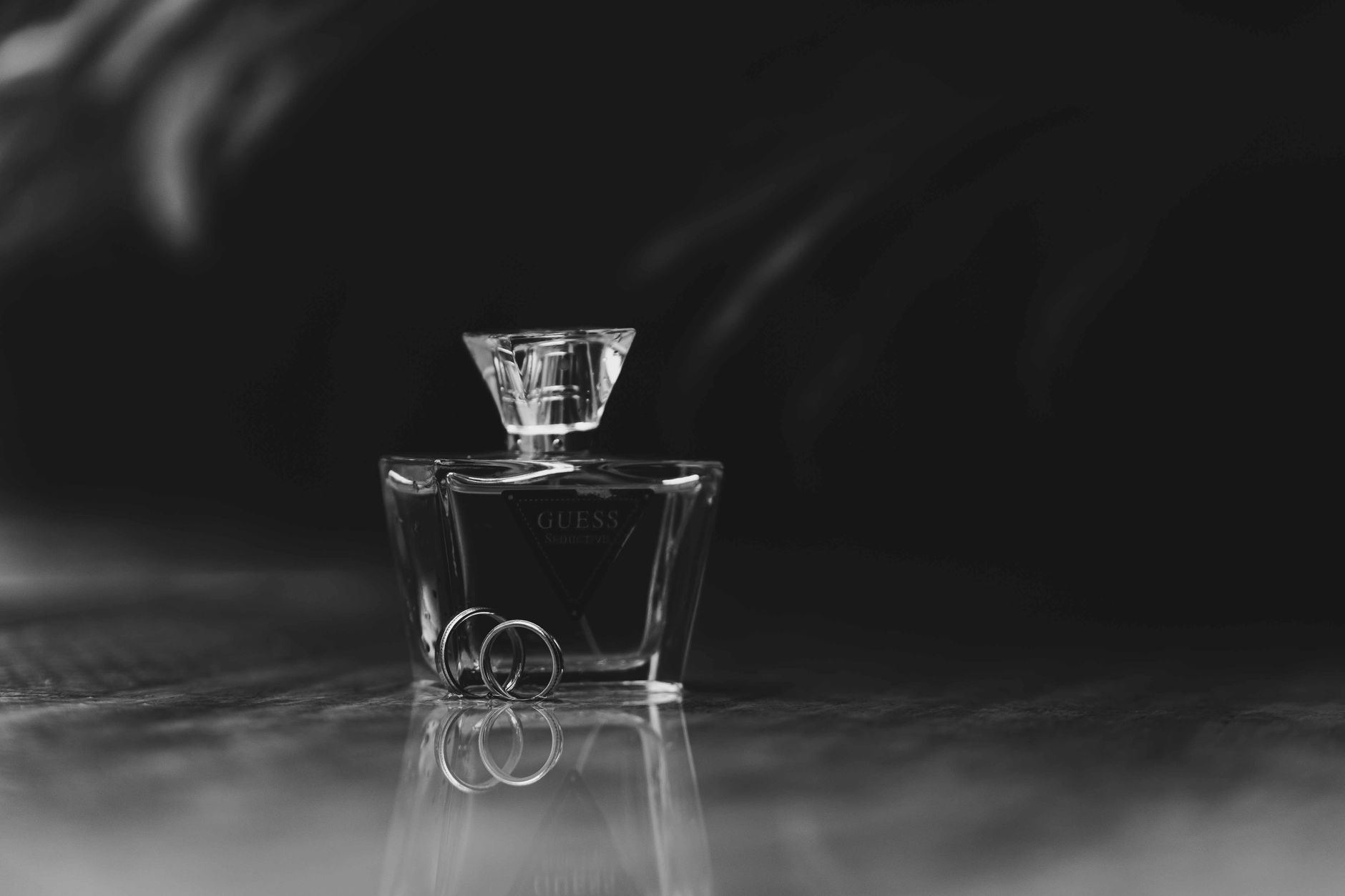Black and white photo of a Guess perfume bottle with wedding rings, highlighting elegance.