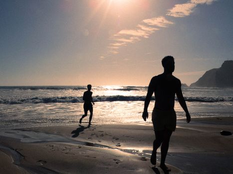 Silhouetted people walking on a beach against a stunning sunset backdrop.