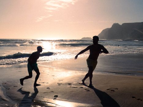 Two people running on a scenic beach at sunset, casting shadows on the sand.