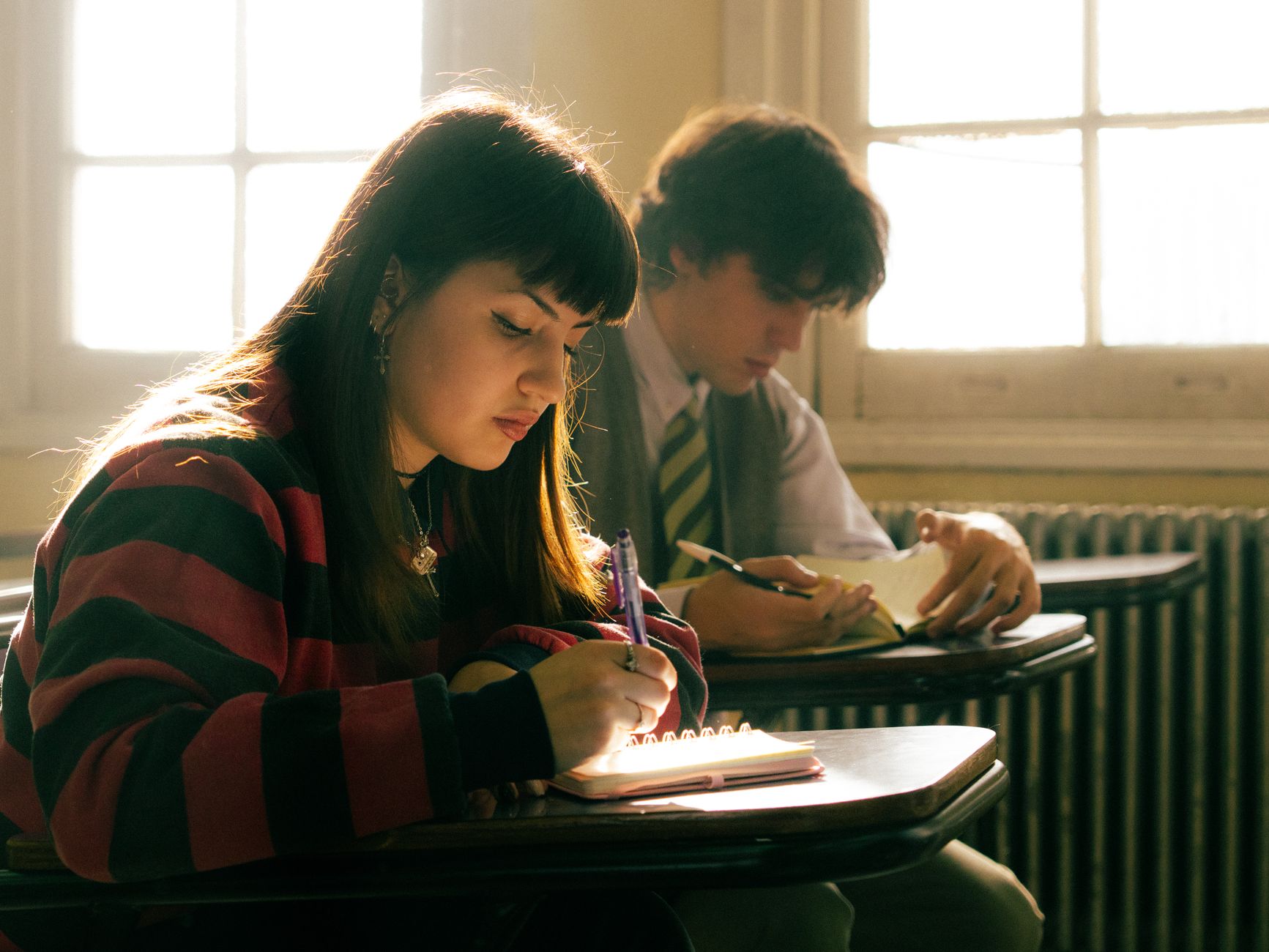 Twee studenten zaten overdag geconcentreerd aantekeningen te maken in een zonnig klaslokaal.