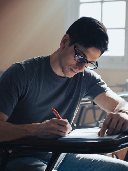 Young man focused on writing an exam in a classroom setting with natural light. Writing A Formal Undergraduate Research: page requirements. - illustration 3