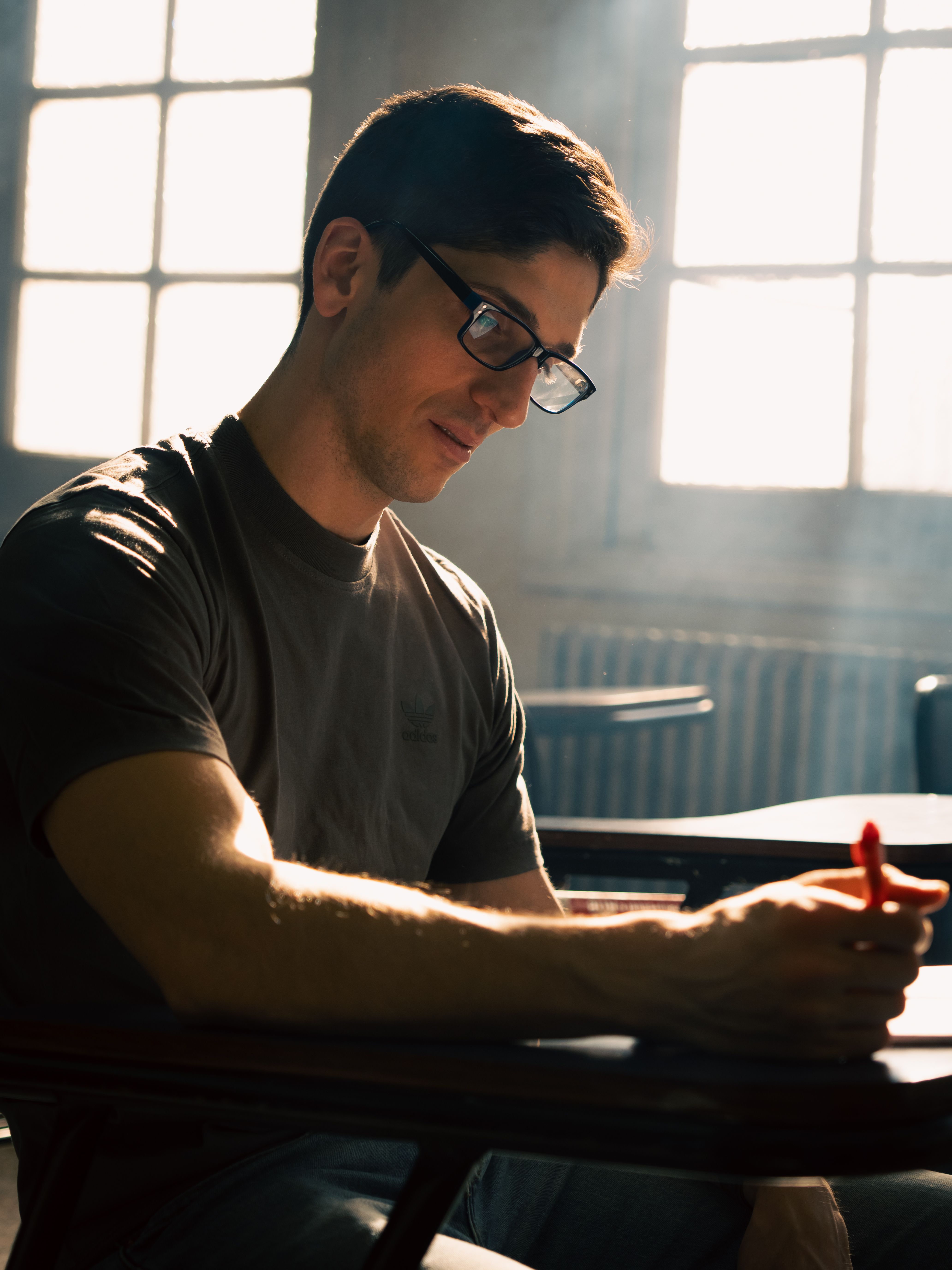 Young man writing at a desk in a Buenos Aires classroom, sunlight streaming through windows.