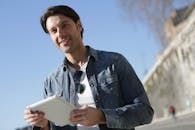 阳光明媚的日子里，一个年轻人在户外微笑着使用平板电脑