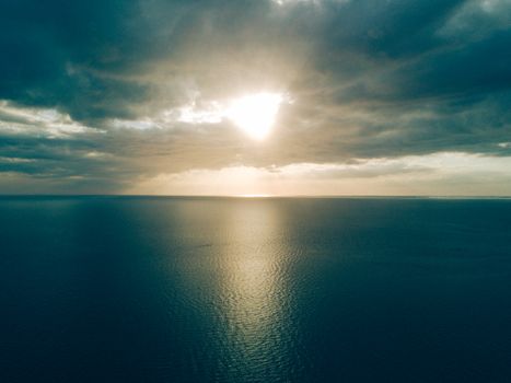 A stunning aerial view of a serene ocean at sunset with dramatic clouds and calm waters.