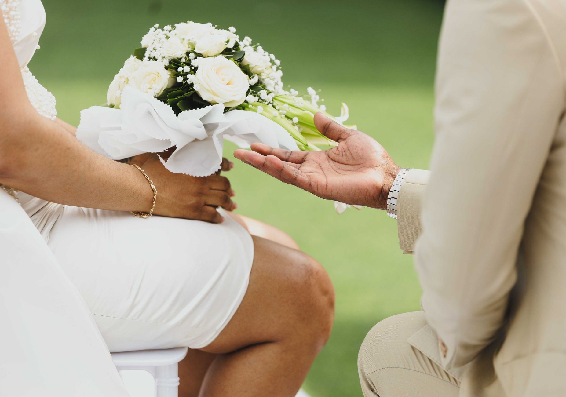 Close-up of a bride and groom in an intimate wedding moment with a bouquet of white flowers outdoors.