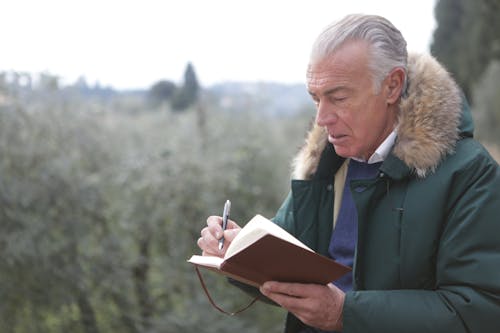 Man in /Green Jacket Holding Pen and Book