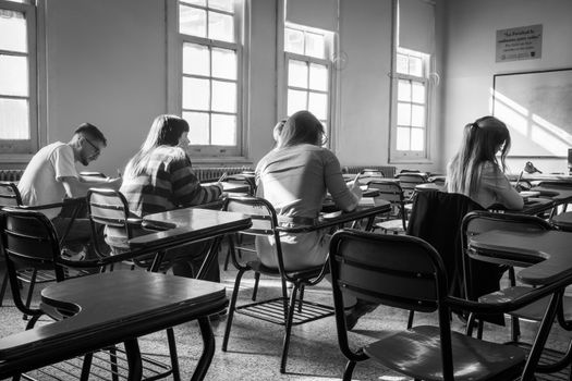 Students studying in a bright, sunlit classroom captured in monochrome.