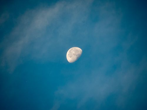 Free A stunning view of a crescent moon set against a bright, clear blue sky with gentle cloud formations. Stock Photo