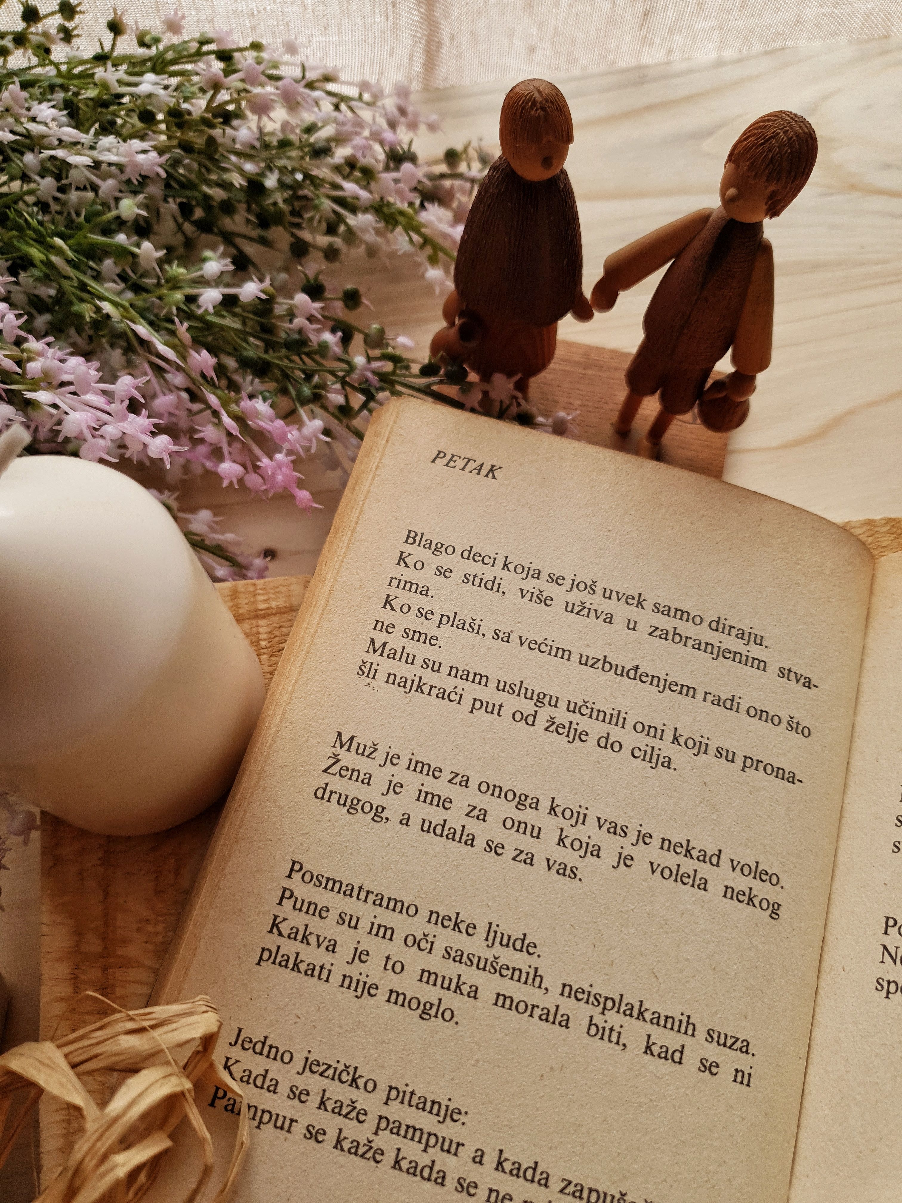 Wooden figures and flowers beside an open book with decorative elements.