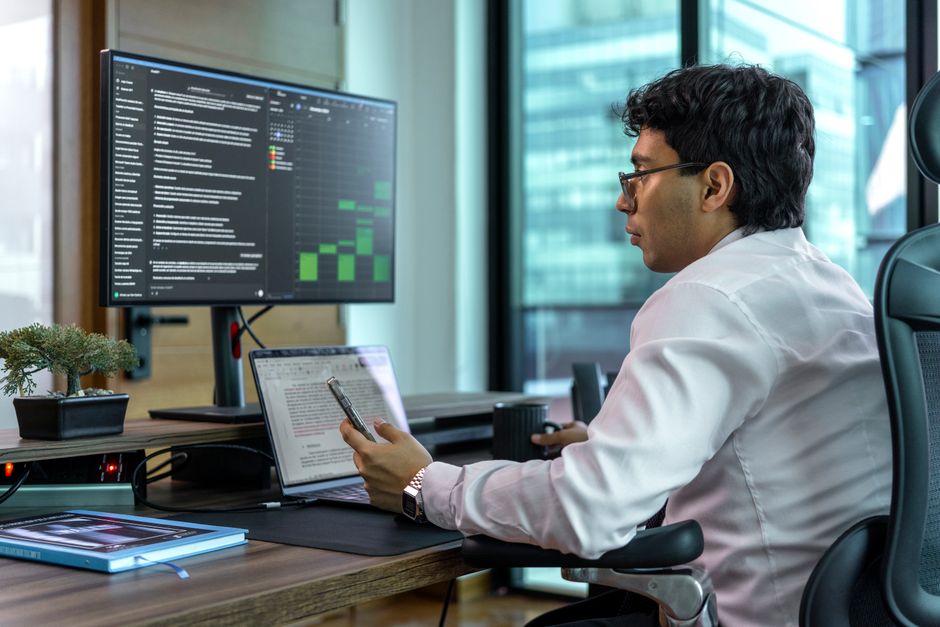 Businessman focused on data analysis on a dual monitor setup in a modern office setting.