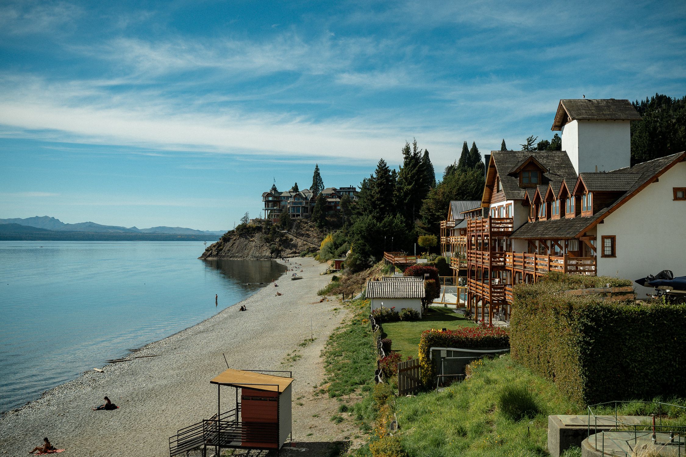 Beautiful lakeside view in Bariloche, Argentina, featuring serene beach, greenery, and charming buildings.