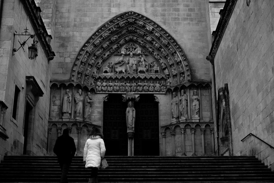 Fotografía en blanco y negro de la entrada de una iglesia gótica con intrincadas esculturas y dos personas ascendiendo.