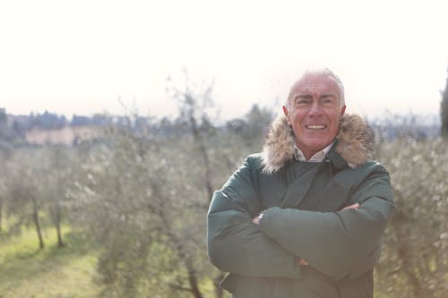 Smiling Man in Green Jacket Standing Near Green Trees