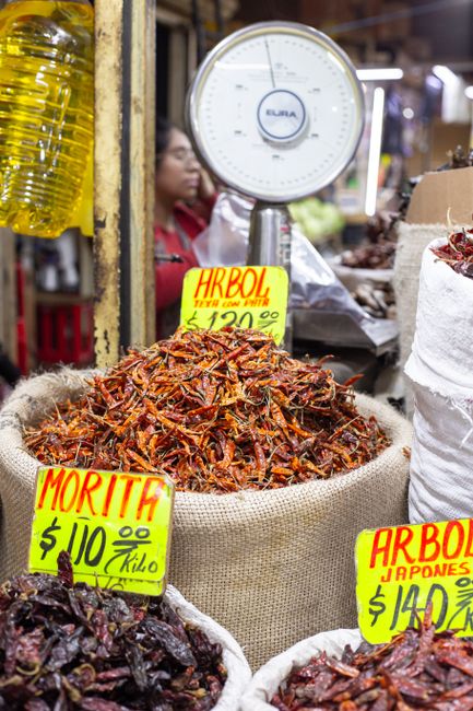 A wooden board with fresh red and green chiles, dried ancho and guajillo pods, and a small pile of crushed red pepper flakes.