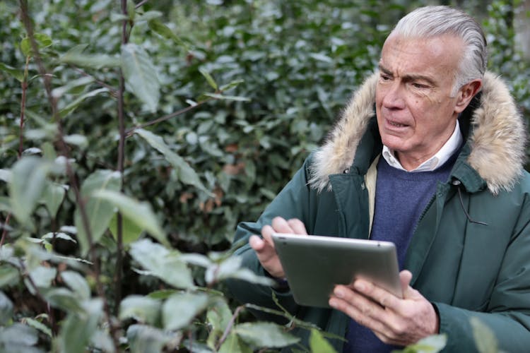 Man In Green Jacket Holding Silver Ipad