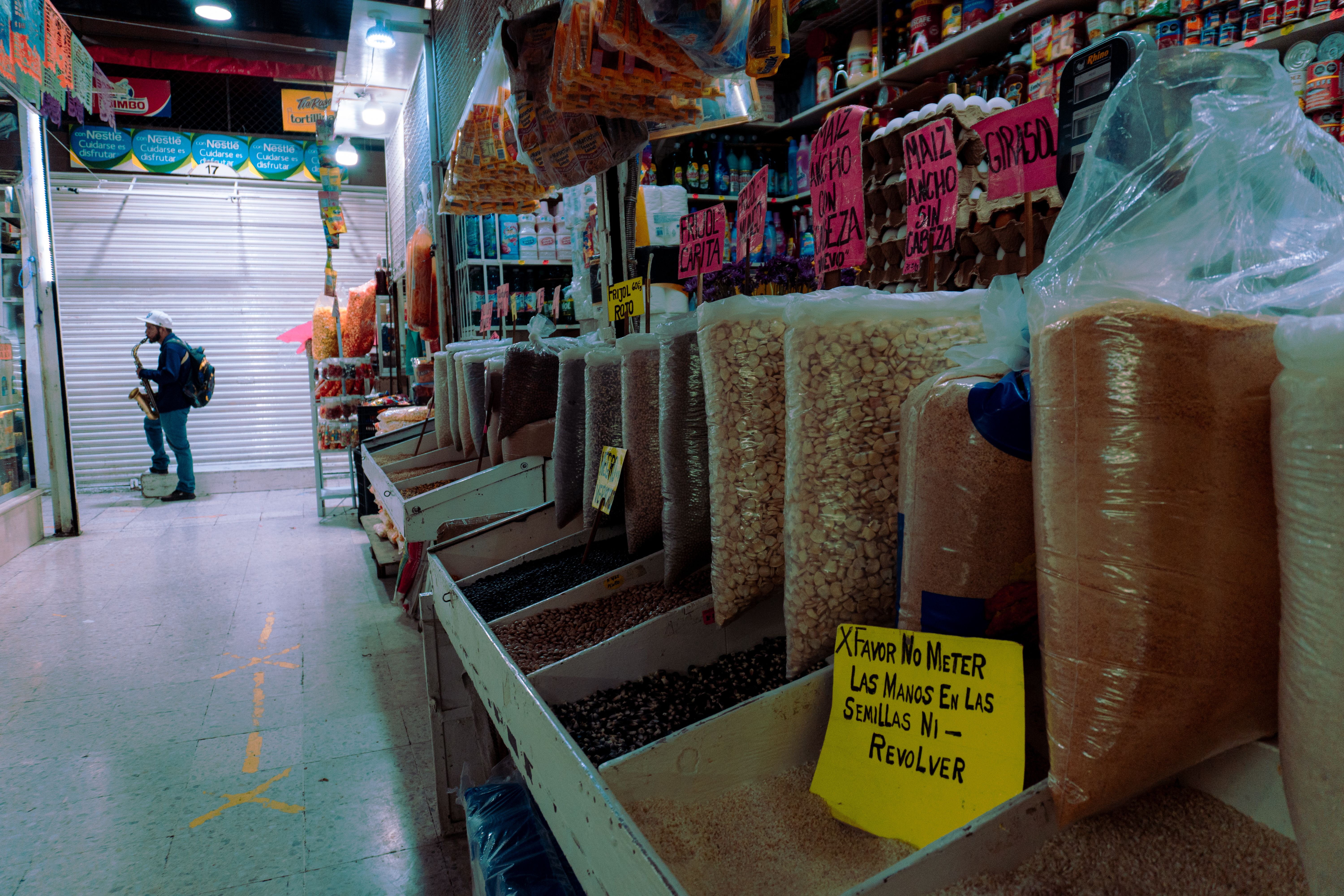 Colorful indoor market scene showcasing various spices and grains with shopper in background.