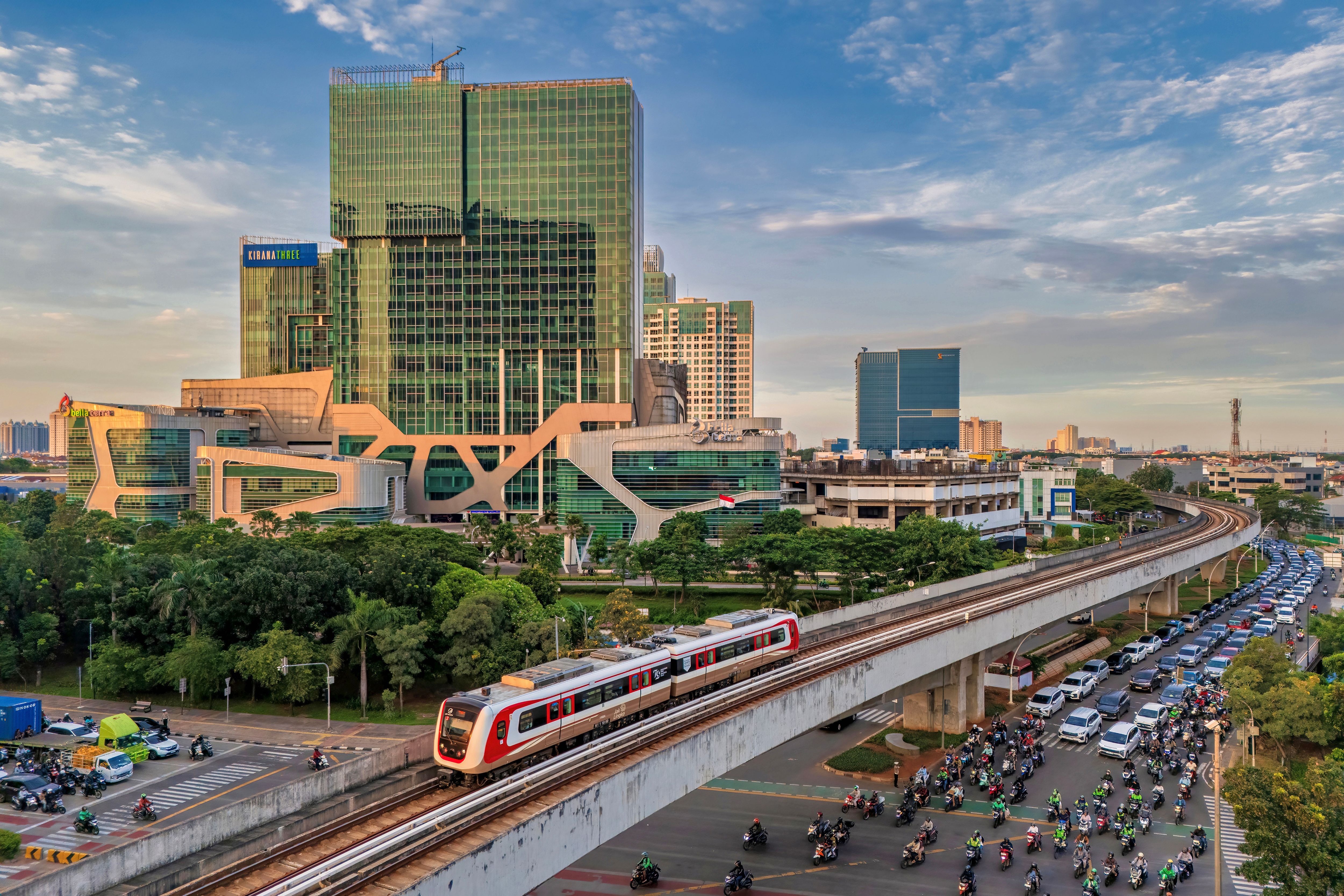Elevated train passing through a bustling Jakarta cityscape with modern buildings under a blue sky.
