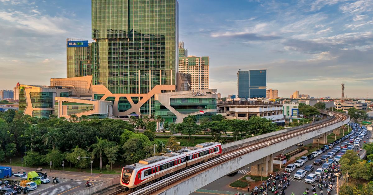 Elevated train passing through a bustling Jakarta cityscape with modern buildings under a blue sky.