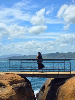 A solitary woman stands on a bridge over the ocean, enjoying the scenic view in New Taipei City, Taiwan.