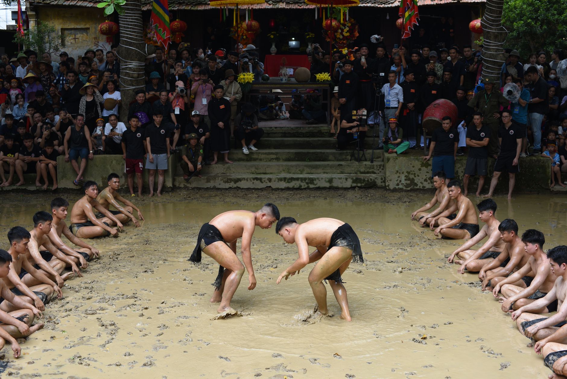 A vibrant traditional mud wrestling festival with enthusiastic participants and spectators in a rural village area.