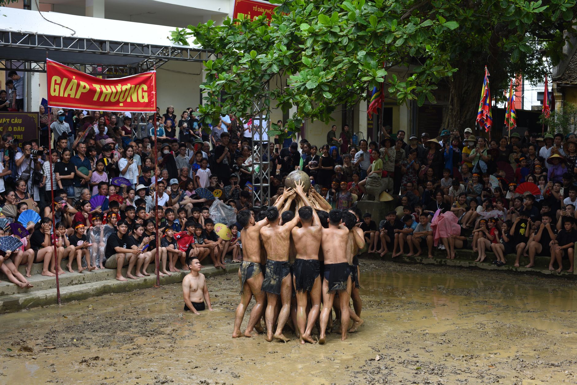 Participants engage in a traditional Vietnamese mud festival, cheered by a large crowd.