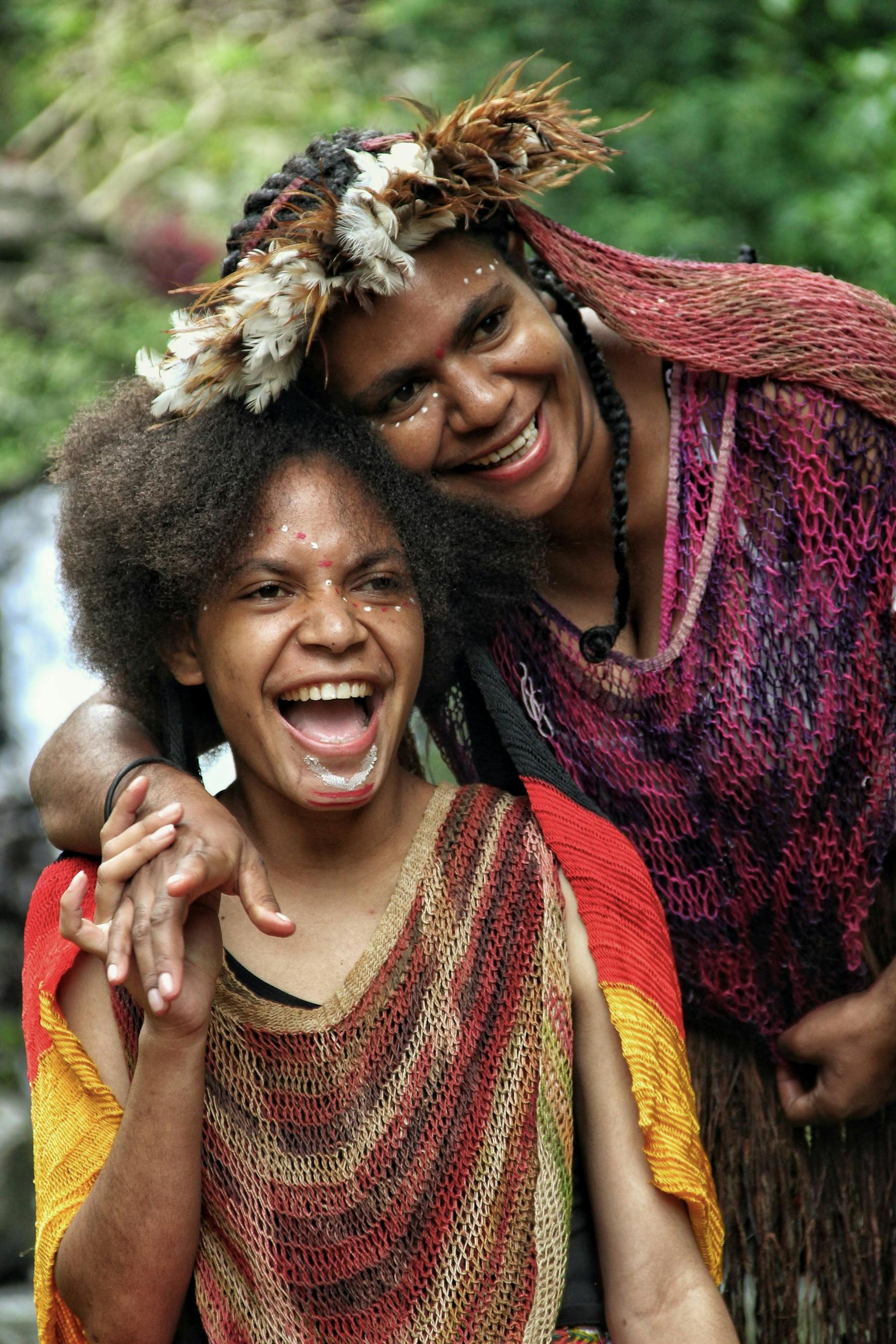 Two women in traditional Indonesian attire share a joyful moment outdoors.