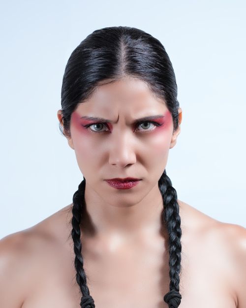 Free A striking portrait of a woman showcasing strong makeup and braided hair against a neutral background. Stock Photo