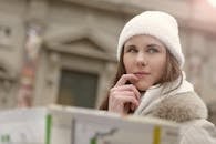 Concentrated female in warm hat and coat looking for right way while standing with map in street