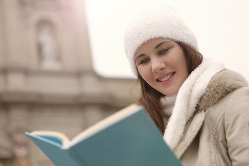 Free From below of smiling female wearing casual warm clothes relaxing in city during weekend and reading interesting book Stock Photo